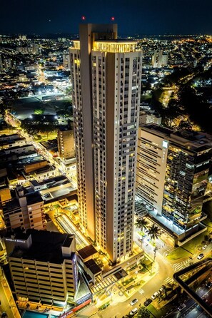 A high-rise hotel with multiple floors, a central courtyard, and a view of the surrounding cityscape at night. - Parking space and view in the tallest building in the city | LYVVO (Campinas)