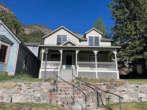 A two-story house with a porch, stone steps, and a mountain backdrop. - This welcoming 4-bedroom house in Ouray is perfect for you. (Ouray)