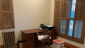 Ein Zimmer mit einem Holztisch, einem Stuhl, einer Heizung und einem Fenster mit Jalousien.