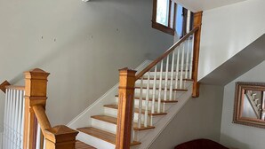 Eine Treppe mit Holzbalkonen und weißen Geländern, die zu einer Zwischenebene mit einem roten Sessel und einem gerahmten Spiegel führt.