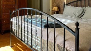 A bedroom with a metal-framed bed, wooden dresser, and patterned wallpaper.