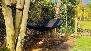A hammock tied between trees in a garden with a dirt path and green grass. - Bendalong  Noordwijk (Noordwijk)