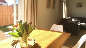 A dining area with a wooden table and chairs, a vase with flowers, and a view of a backyard. - Bendalong  Noordwijk (Noordwijk)