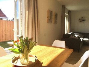 Ein Essbereich mit einem Holztisch und Stühlen, einer Vase mit Blumen und Blick auf einen Garten.