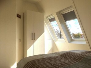 Ein Schlafzimmer mit Oberlicht, Kleiderschrank und einem Bett mit gemustertem Überwurf.
