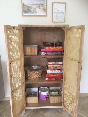Ein Holzkabinent mit geöffneten Türen, gefüllt mit Gesellschaftsspielen und einem gewebten Korb.