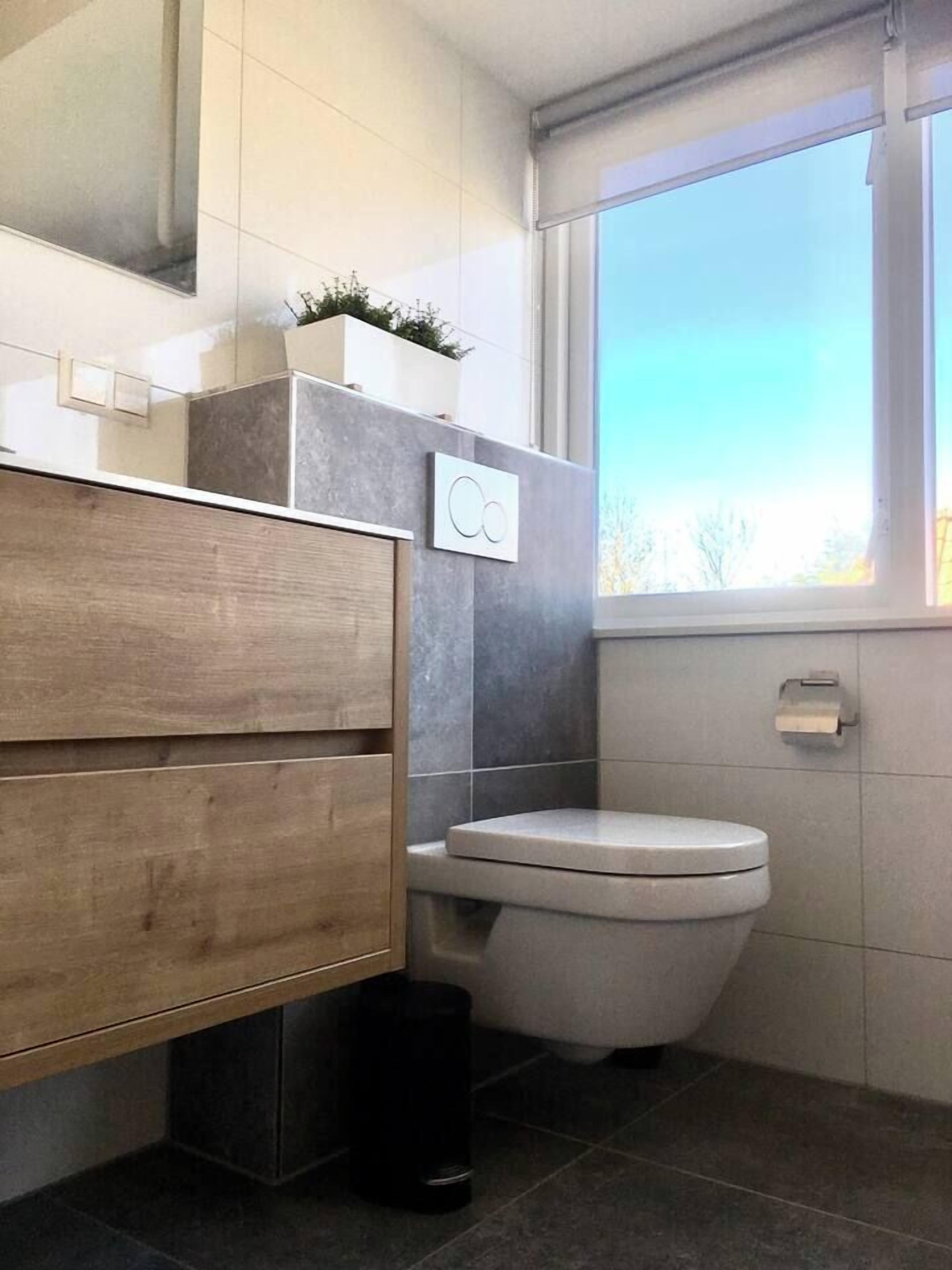Ein modernes Badezimmer mit einem hölzernen Waschtisch, einer weißen Toilette und einem Fenster mit Tageslicht.