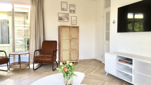A living room with a TV, a brown armchair, a white sofa, a small table, and a cabinet with shelves. - Bendalong  Noordwijk (Noordwijk)