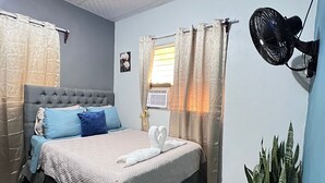 Ein Schlafzimmer mit einem Bett, einem Standventilator, einer Zimmerpflanze und einem Fliesenboden mit Muster.