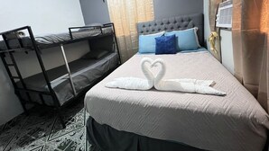 Ein Einzelbett mit gestepptem Kopfteil, ein Hochbett zur Linken und eine Wand-Klimaanlage.