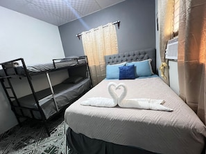 Un lit simple avec une tête de lit matelassée, un lit superposé à gauche et un climatiseur fixé au mur.