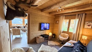 Interior de una cabaña de madera con un venado montado en la pared, un televisor, un sofá y una silla.