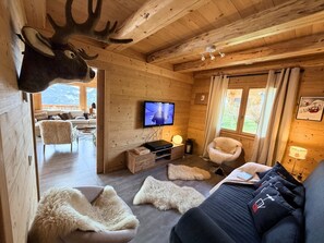 Ein Interieur einer Holzhütte mit einem aufgehängten Hirschgeweih, einem Fernseher, einem Sofa und einem Sessel.