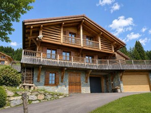 A two-story wooden house with a stone facade, a balcony, and a garage. - Luxury Chalet "La Framboiseille" with Pool and Sauna (Manigod)