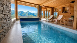Una piscina interior con agua azul cristalina, paredes de madera y vistas a montañas.