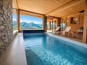 Ein Hallenbad mit klarem, blauen Wasser, Holzwänden und Blick auf Berge.