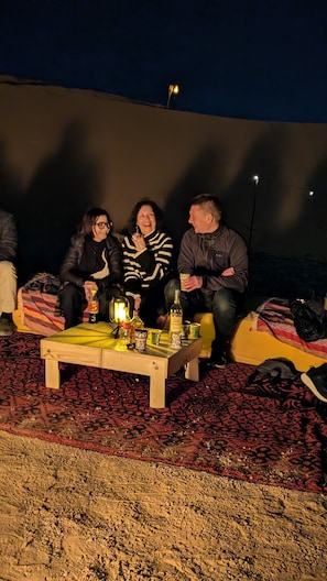 A group of people seated on a couch with a table in front of them, holding drinks and a bottle.