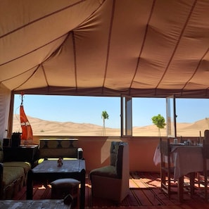 A tented room with a table, chairs, and a view of the desert.
