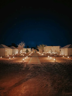 A series of tents arranged in a row with a pathway leading through them, under a night sky.