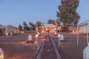 A desert-style venue with a central pathway leading to a building, surrounded by trees and illuminated by lanterns.