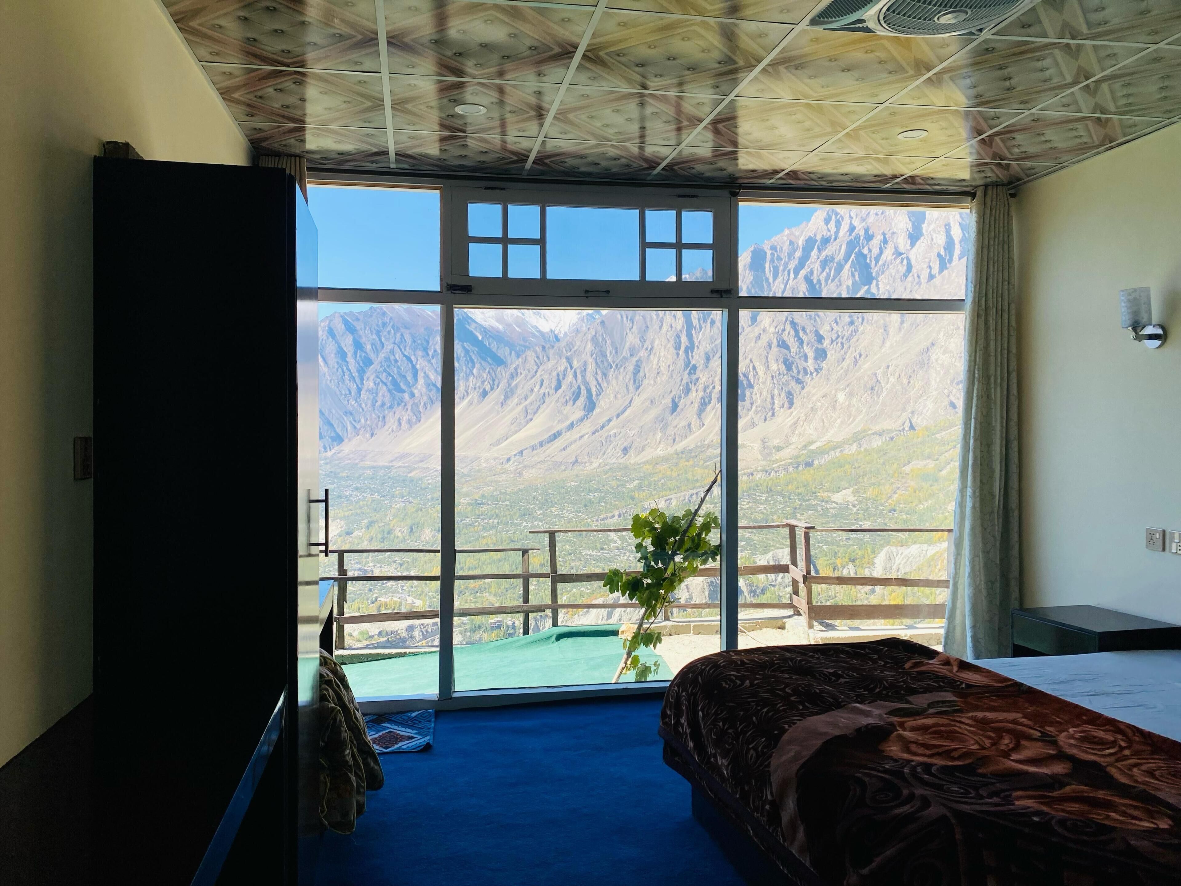 A room with a bed, a desk, and a large window with a mountain view.