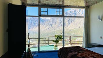 A room with a bed, a desk, and a large window with a mountain view.