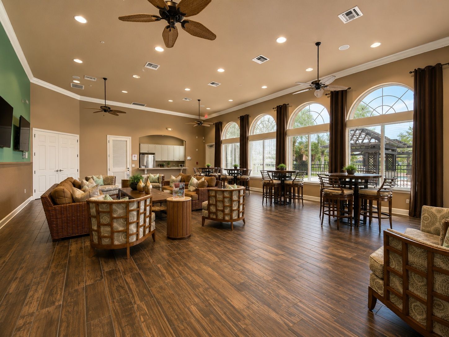 A spacious living area with a high ceiling, multiple ceiling fans, and large windows providing natural light.