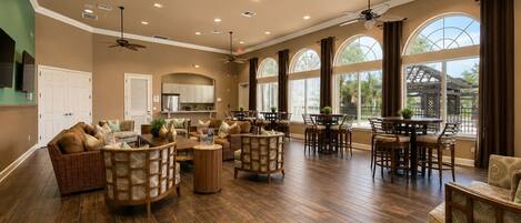 A spacious living area with a high ceiling, multiple ceiling fans, and large windows providing natural light.