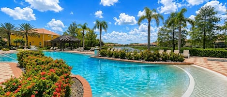 A clear blue pool with a brick border, surrounded by palm trees and a gazebo.