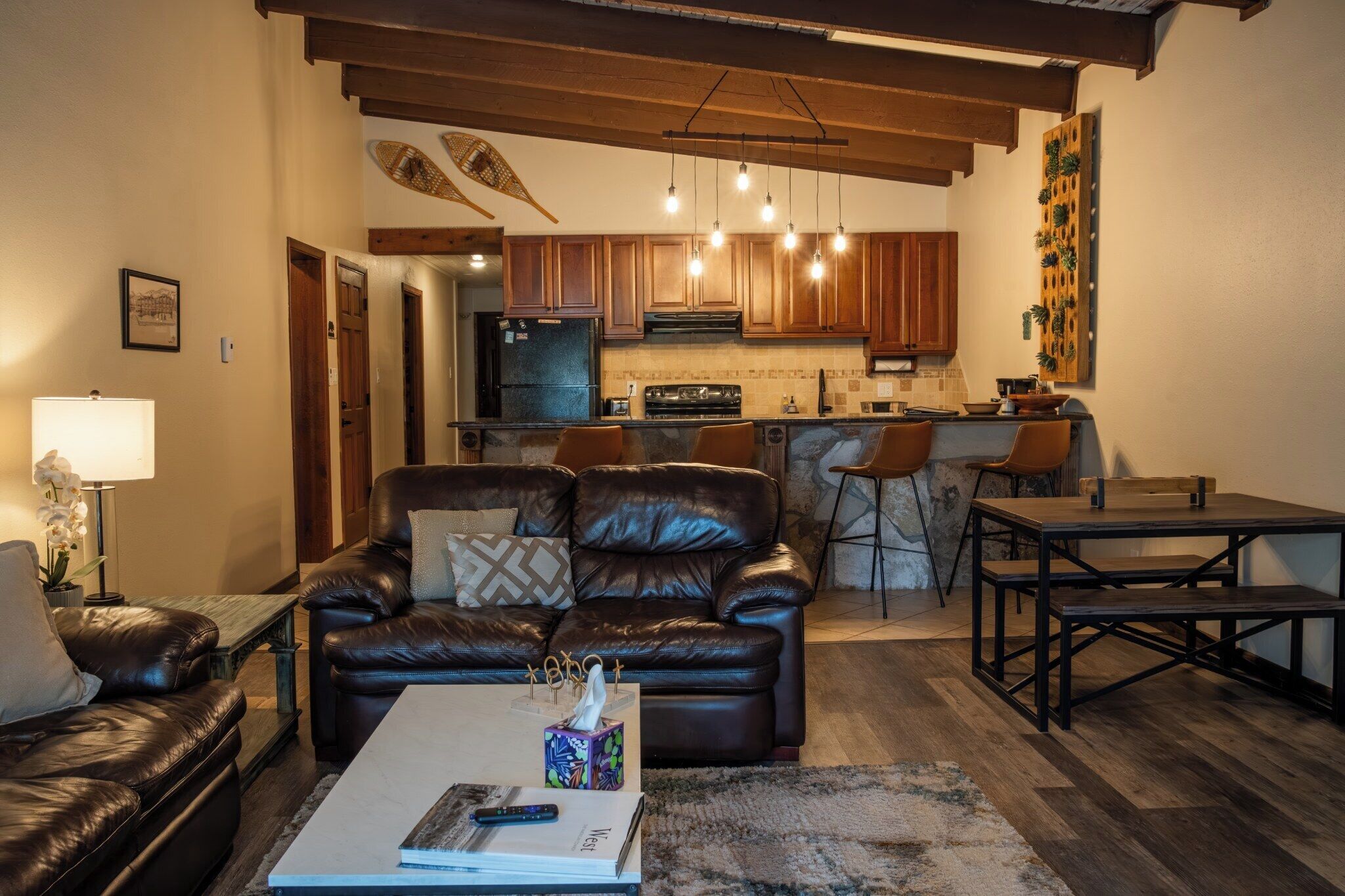Una sala de estar con un sofá de cuero, una mesa de centro y una cocina al fondo.