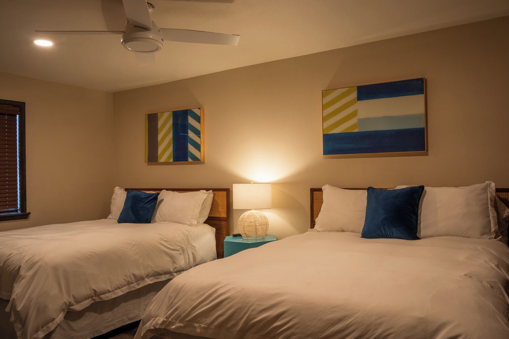 A hotel room with two beds, a ceiling fan, and artwork on the walls.