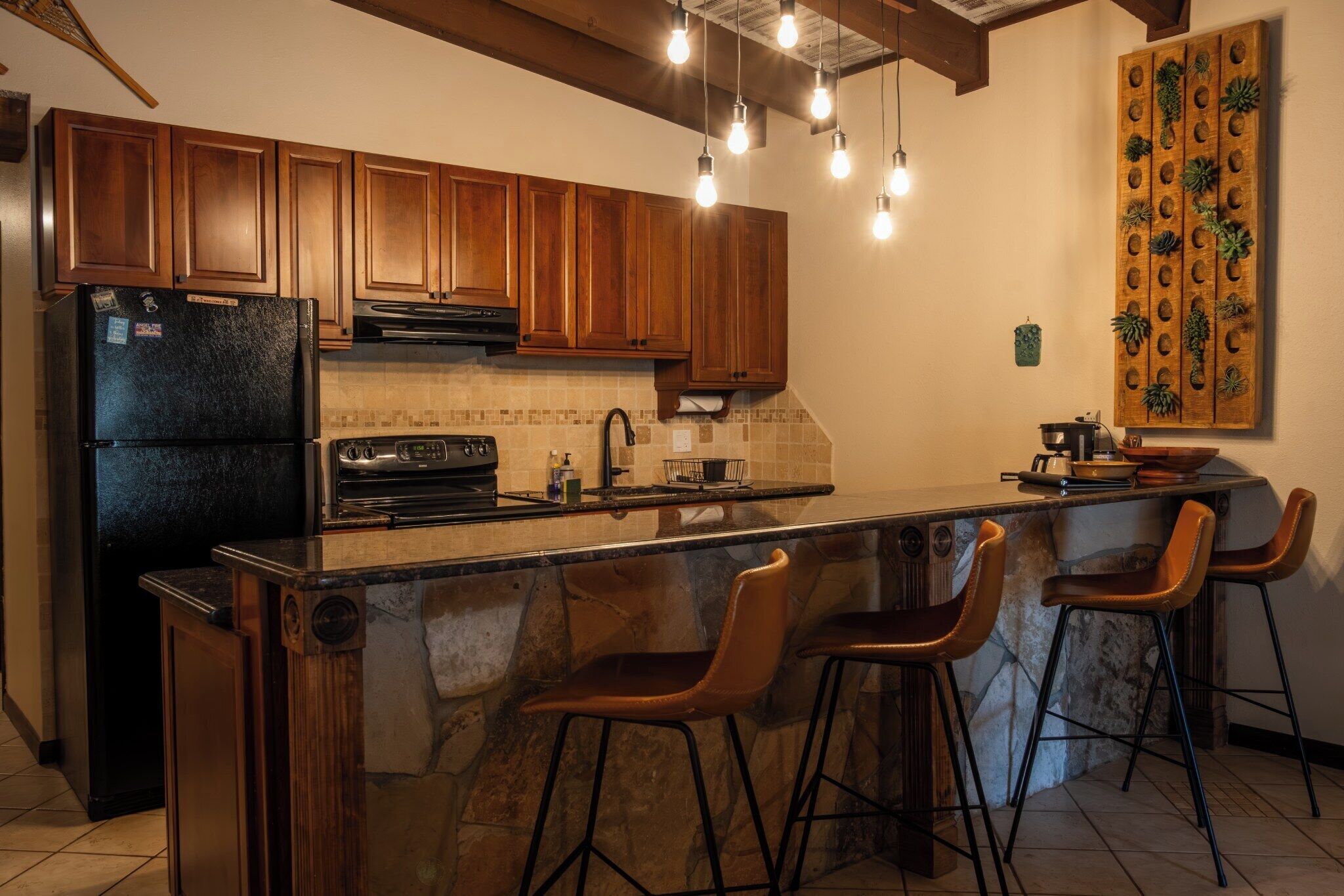 A kitchen with wooden cabinets, a black refrigerator, a stove, a sink, and bar stools.