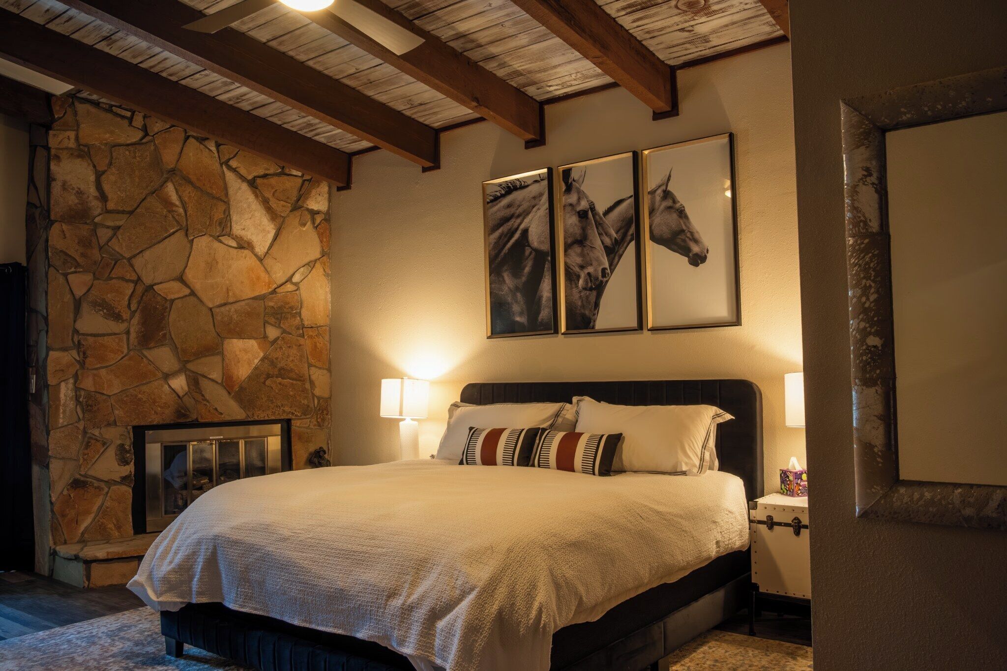 Ein Schlafzimmer mit einer Steinwand, einem Bett mit Kopfteil und zwei gerahmten Bildern von Pferden.