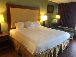 Una cama grande con cabecera de madera, dos lámparas de noche, una mesita y una silla estampada.