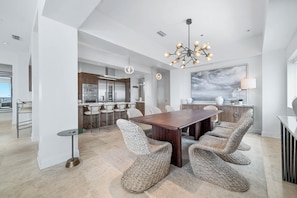 A modern kitchen with built-in appliances, a dining area with wicker chairs, and a large painting on the wall.