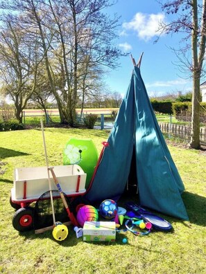 A tent set up on grass with a wheelbarrow, sports balls, and a badminton racket nearby. - Maralong in Noordwijk (Noordwijk)