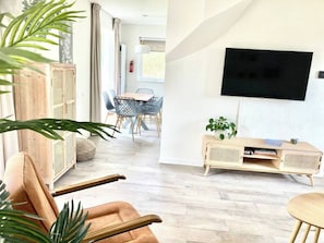 A modern living room with a flat-screen TV mounted on the wall, a wooden entertainment unit, and a dining area with a table and chairs. - Maralong in Noordwijk (Noordwijk)