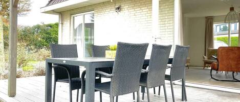 Un patio al aire libre con una mesa y sillas, una zona cubierta con techo y vistas al paisaje circundante.