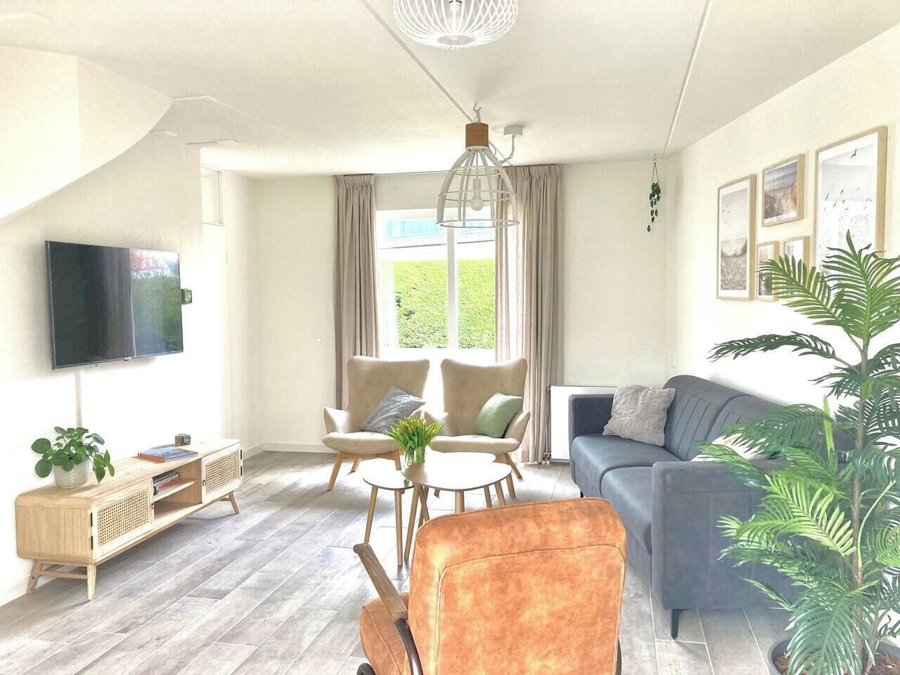 Ein Wohnzimmer mit einer Couch, Sesseln, einem Fernseher und einer Pflanze.