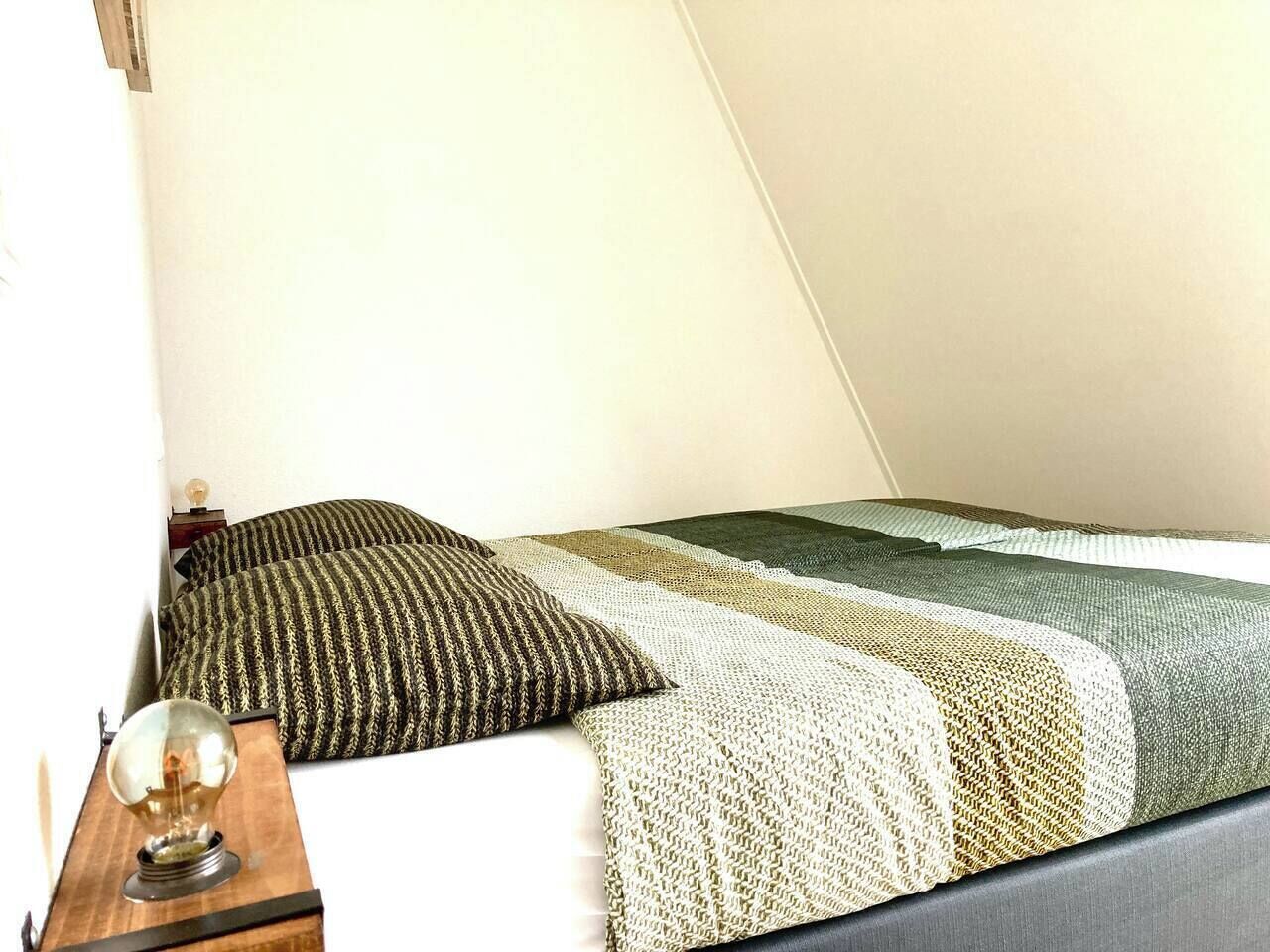 A room with a bed, pillows, a bedside table, and a lamp.