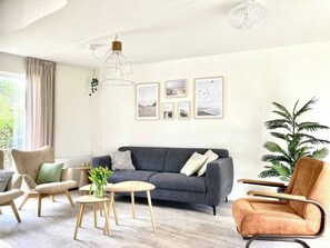 Een moderne woonkamer met een grijze bank, twee fauteuils, een bijzettafeltje en een potplant.