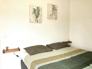 A bed with a patterned bedspread, two pillows, a bedside table with a lamp, and two wall-mounted artworks. - Maralong in Noordwijk (Noordwijk)