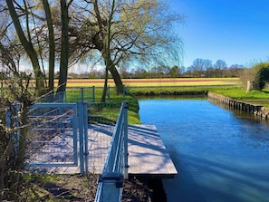 A riverside walkway with a wooden dock, surrounded by trees and a clear sky. - Maralong Noordwijk (Noordwijk)