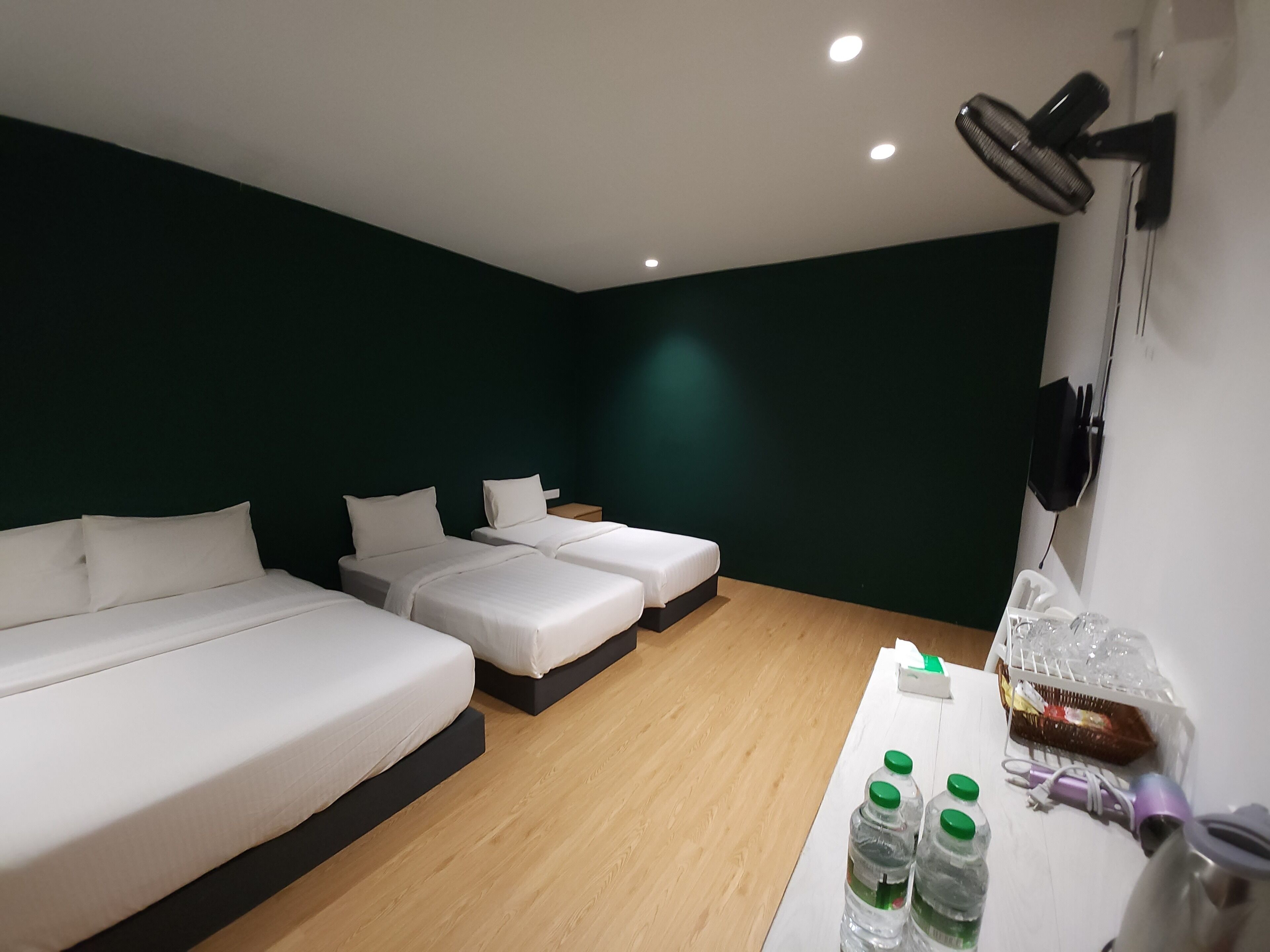 Ein Hotelzimmer mit zwei Betten, Holzboden, einem Tisch mit Wasserflaschen und einem Föhn.