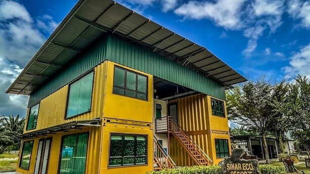 A two-story building with a green roof and yellow walls, featuring a staircase and a sign that reads 'SINAR ECO RESORT'.