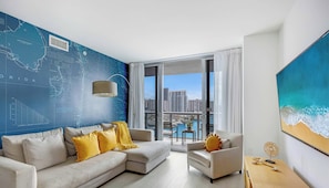 A modern living room with a large window, a city view, and a wall with a nautical-themed map. - Luxurious Intracoastal - 2BR Upper Beachwalk Suite (Hallandale Beach)