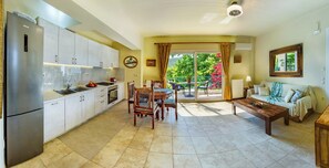 A modern kitchen with a refrigerator, stove, and sink. There is a dining area with a table and chairs. The room has a large window with a view of greenery. - Lefkas Blue Residence Two-bedroom Suite near to the town and close to the beach. (Lefkada)