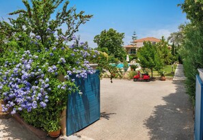 A gated driveway with a blue gate, a red scooter, and a pool area in the background. - Lefkas Blue Residence Two-bedroom Suite near to the town and close to the beach. (Lefkada)