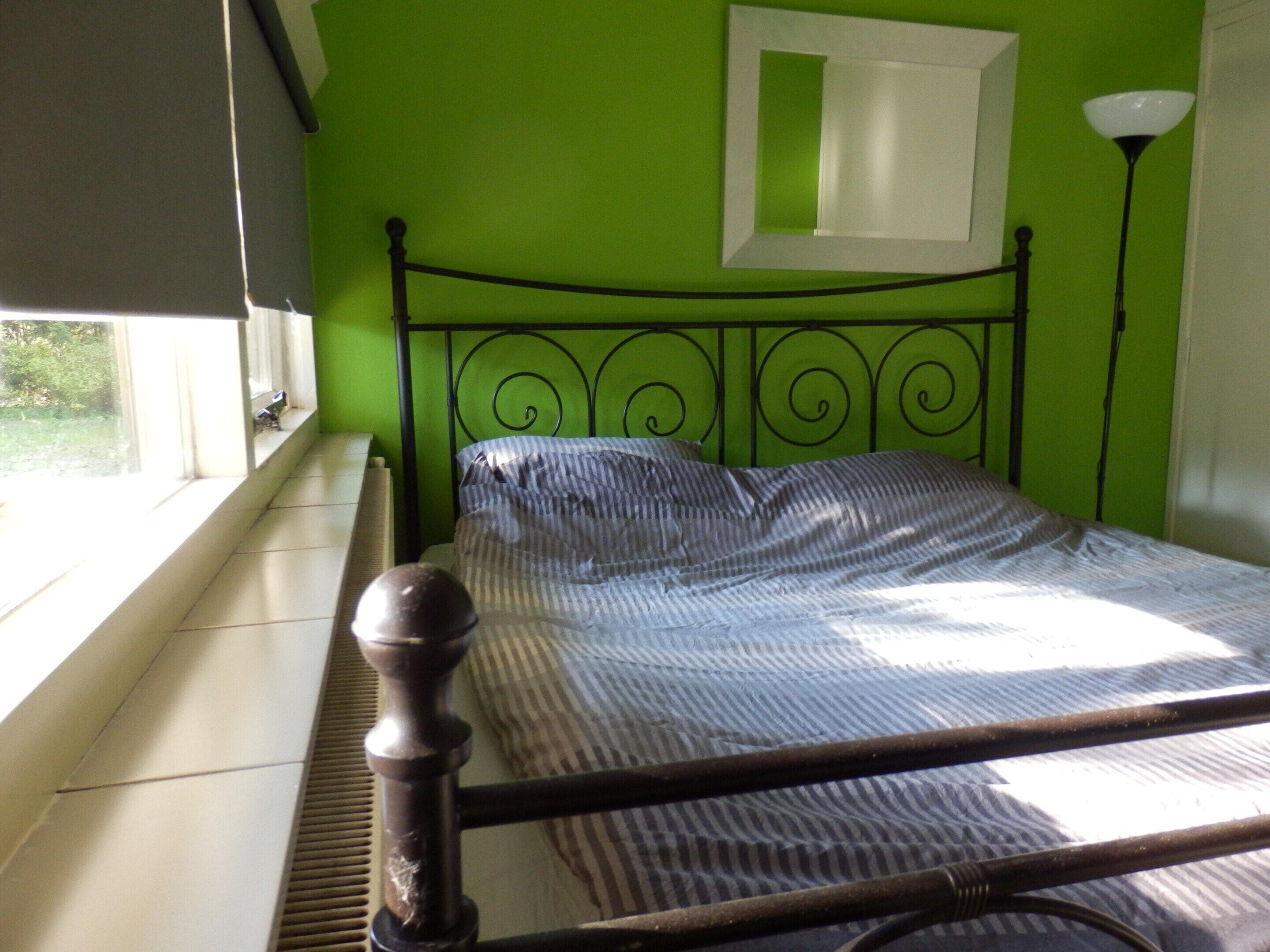 A bed with a metal headboard, a window with blinds, and a green wall.