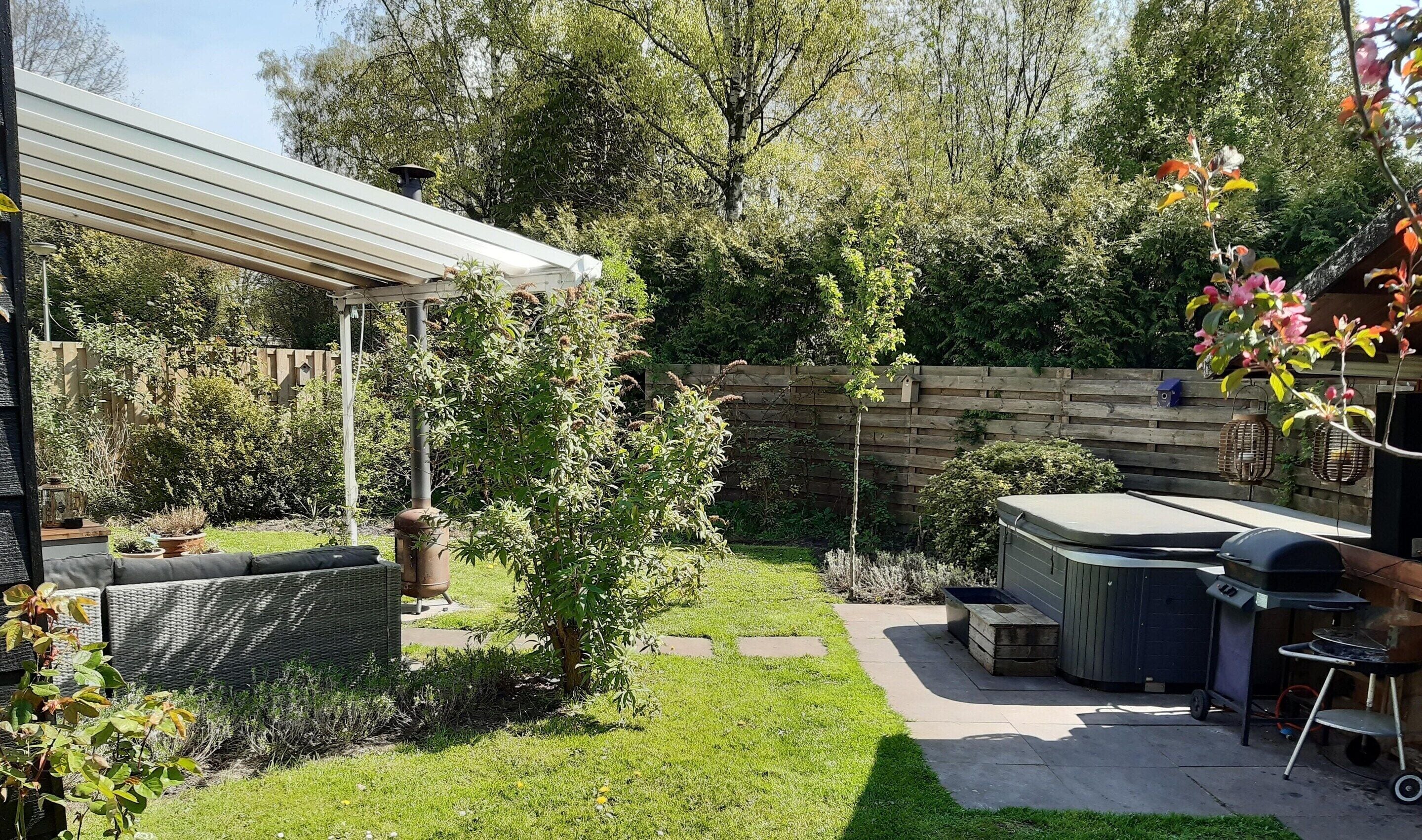 A backyard with a covered patio, a grill, and a wooden fence.
